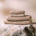 NUDA Bamboo Waffle Bath Towel Set in warm oatmeal and sand tones on natural stone